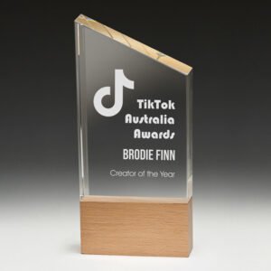 Angled clear glass corporate awards trophy with engraved text mounted on natural timber base
