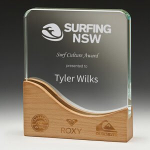 Curved clear glass corporate awards trophy with engraved surf award text mounted on wave shaped timber base