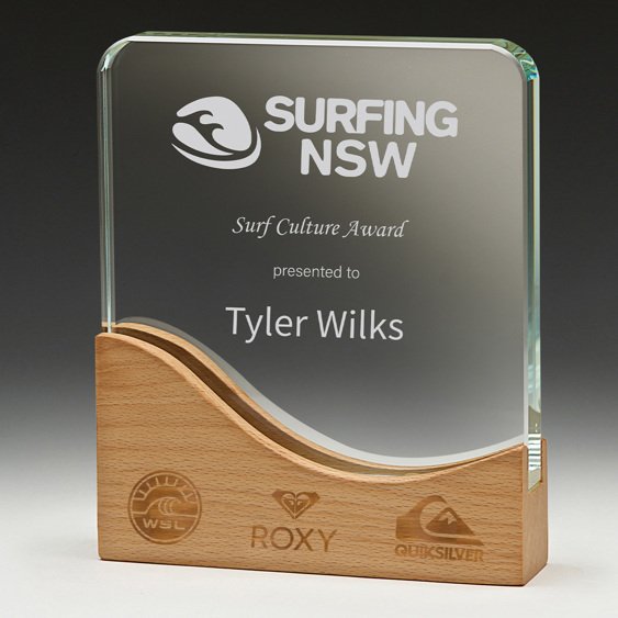 Curved clear glass corporate awards trophy with engraved surf award text mounted on wave shaped timber base