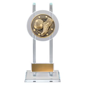 Small clear glass award with twin upright panels and circular soccer medal featuring boot and ball design, mounted on glass base with gold engraving plate.