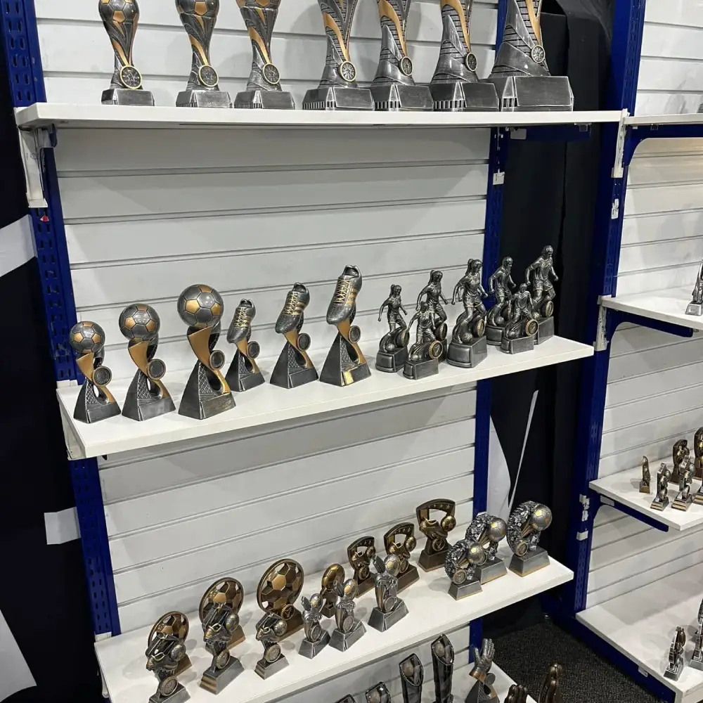 Display shelves filled with soccer trophies and football award statues in various sizes and designs inside awards showroom